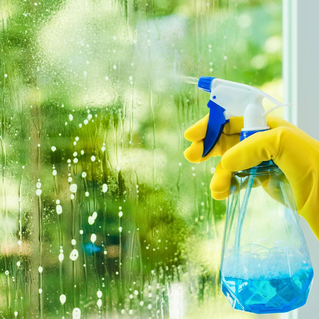 a hand with industrial gloves spraying a window with cleaning product